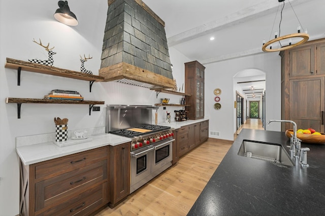 kitchen featuring sink, light hardwood / wood-style flooring, beamed ceiling, decorative light fixtures, and range with two ovens