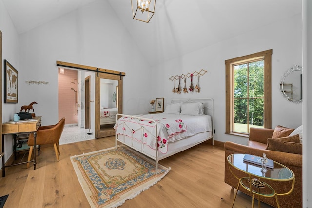 bedroom featuring a barn door, an inviting chandelier, high vaulted ceiling, and hardwood / wood-style flooring