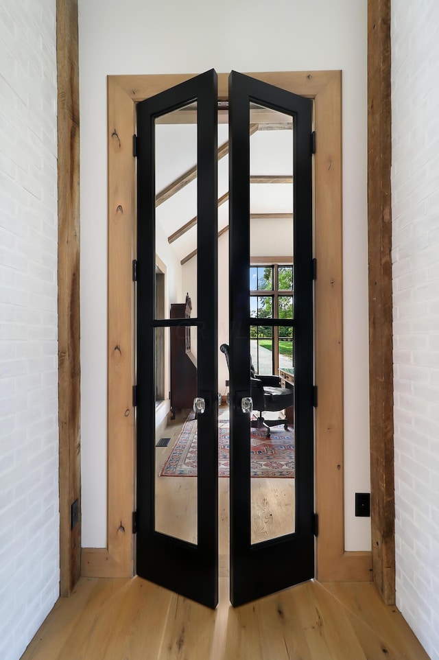 doorway to outside featuring wood-type flooring, french doors, and brick wall