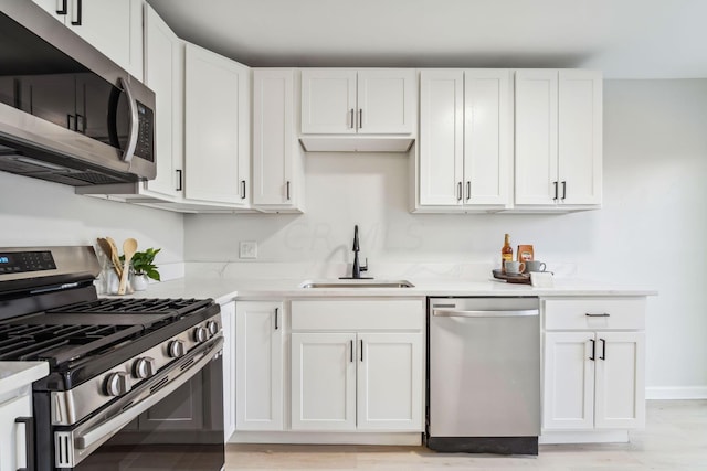 kitchen with white cabinets, stainless steel appliances, light hardwood / wood-style floors, and sink