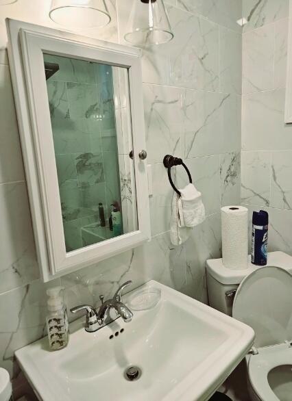 bathroom featuring toilet, sink, tasteful backsplash, and tile walls