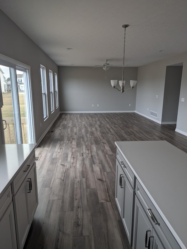 unfurnished dining area with ceiling fan with notable chandelier and dark wood-type flooring