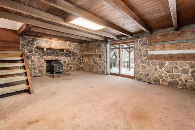 unfurnished living room with carpet flooring, a wood stove, beamed ceiling, and wood ceiling