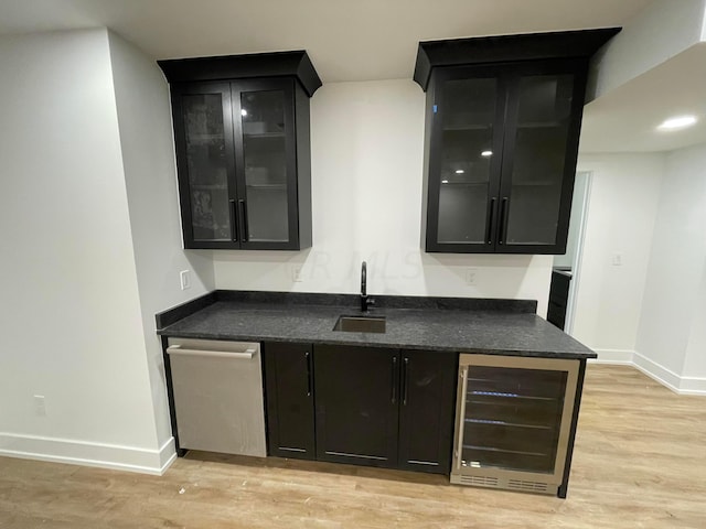 bar featuring stainless steel dishwasher, sink, beverage cooler, and light hardwood / wood-style flooring