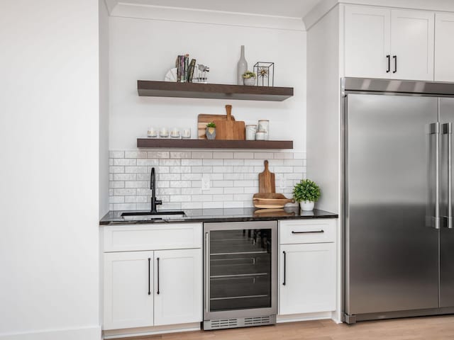 bar with sink, white cabinets, beverage cooler, and stainless steel built in refrigerator