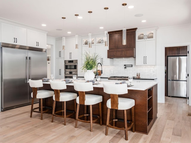 kitchen with a center island with sink, pendant lighting, custom range hood, and appliances with stainless steel finishes