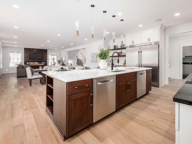 kitchen featuring stainless steel appliances, decorative light fixtures, light hardwood / wood-style floors, white cabinetry, and an island with sink