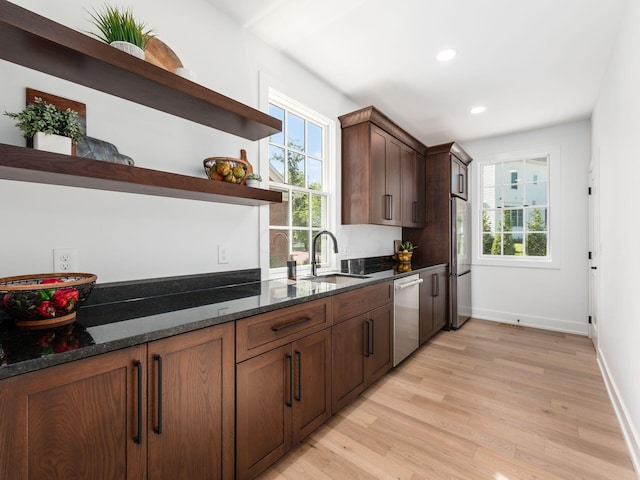 kitchen with sink, stainless steel appliances, dark stone counters, and light hardwood / wood-style flooring