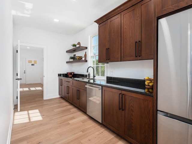 kitchen featuring dark brown cabinetry, sink, light hardwood / wood-style flooring, dark stone counters, and appliances with stainless steel finishes