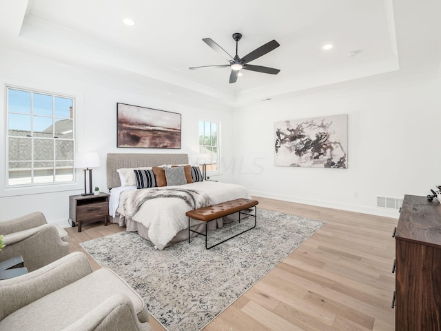 bedroom featuring light wood-type flooring, a tray ceiling, and ceiling fan