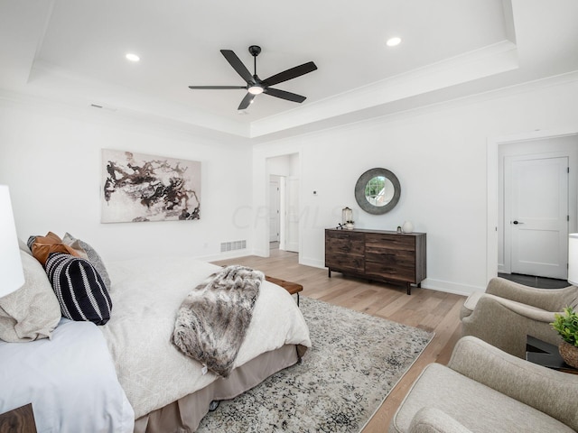 bedroom with light wood-type flooring, a raised ceiling, ceiling fan, and ornamental molding