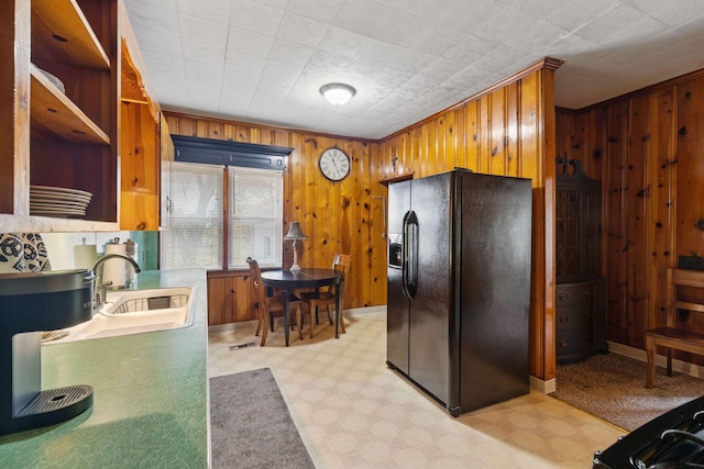 kitchen featuring black fridge with ice dispenser, sink, and wooden walls