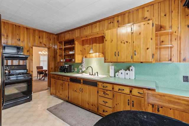 kitchen with crown molding, sink, black appliances, a notable chandelier, and wood walls