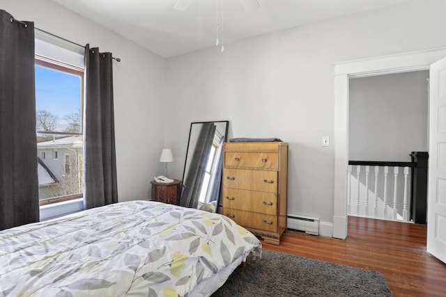 bedroom with ceiling fan, dark hardwood / wood-style flooring, and a baseboard heating unit