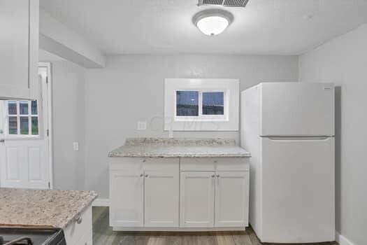 kitchen with white refrigerator, white cabinetry, light stone countertops, and light hardwood / wood-style floors