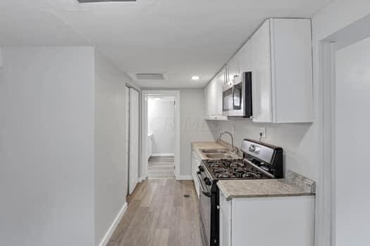 kitchen with light wood-type flooring, stainless steel appliances, sink, and white cabinets