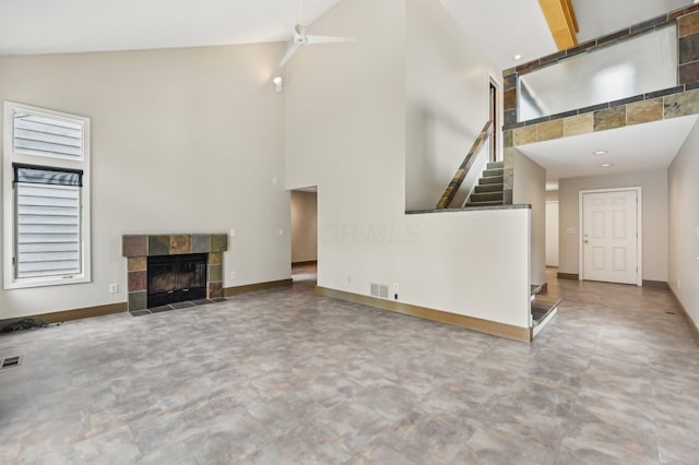 unfurnished living room featuring a tile fireplace, visible vents, a towering ceiling, and baseboards