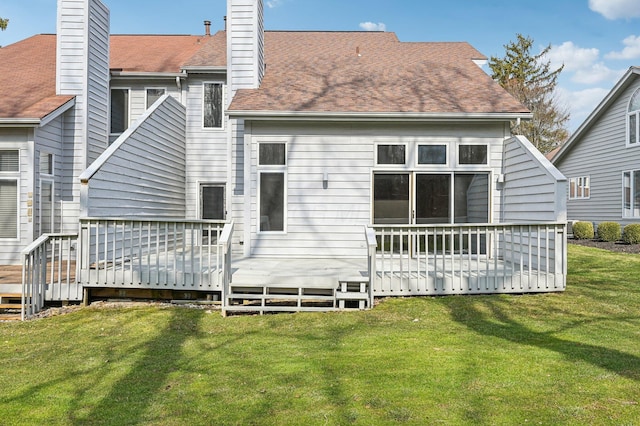 rear view of property with a shingled roof, a chimney, a deck, and a yard