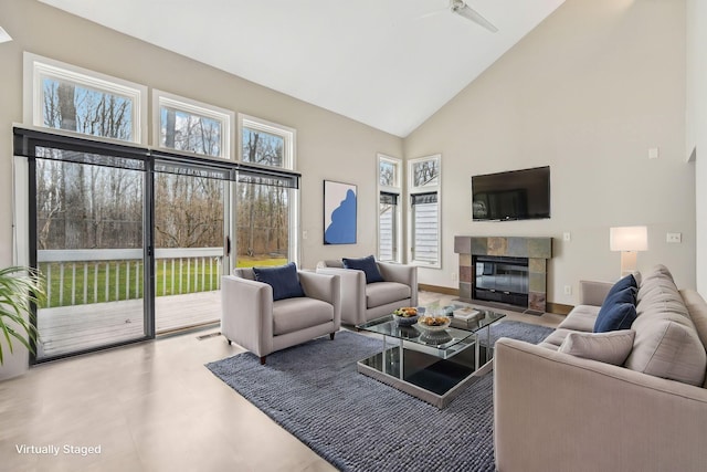 living room featuring a tiled fireplace, high vaulted ceiling, plenty of natural light, and baseboards