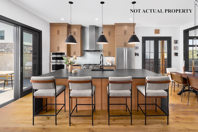 kitchen with dark countertops, wall chimney exhaust hood, modern cabinets, a kitchen island with sink, and stainless steel appliances