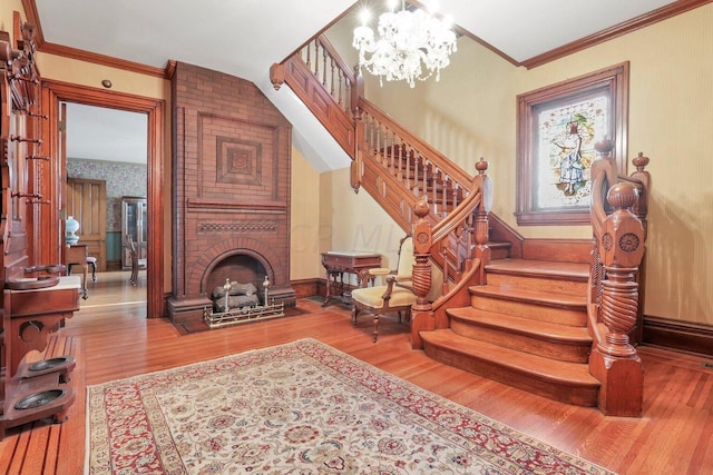 stairway with a fireplace, ornamental molding, hardwood / wood-style flooring, and a notable chandelier