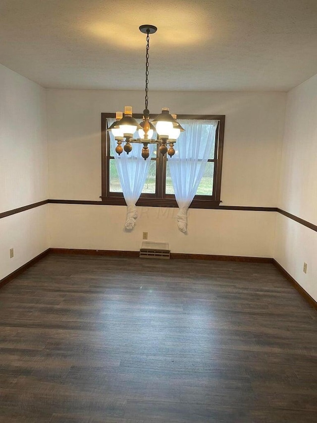 spare room with a textured ceiling, dark hardwood / wood-style flooring, a healthy amount of sunlight, and a notable chandelier