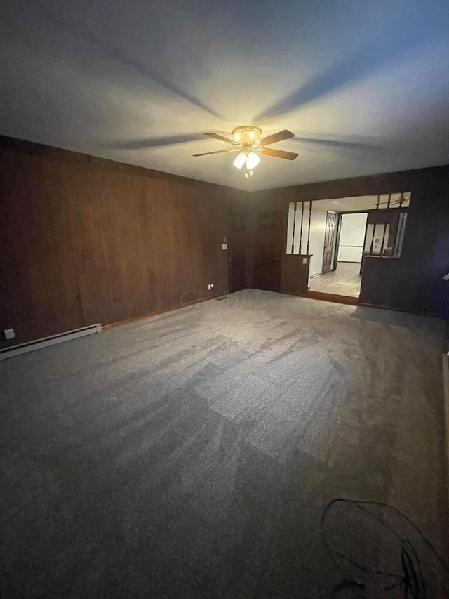 carpeted spare room with baseboard heating, wooden walls, and ceiling fan