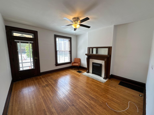 unfurnished living room featuring dark hardwood / wood-style flooring, a brick fireplace, plenty of natural light, and ceiling fan