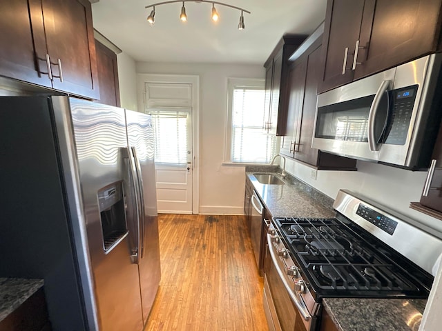 kitchen featuring sink, appliances with stainless steel finishes, light wood-type flooring, and dark stone countertops