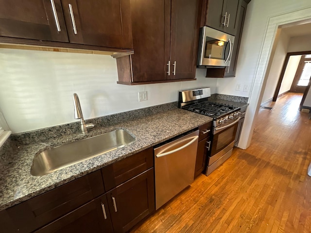 kitchen featuring dark stone countertops, hardwood / wood-style floors, stainless steel appliances, and sink