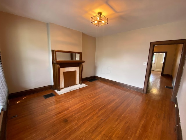 unfurnished living room featuring a brick fireplace and dark wood-type flooring