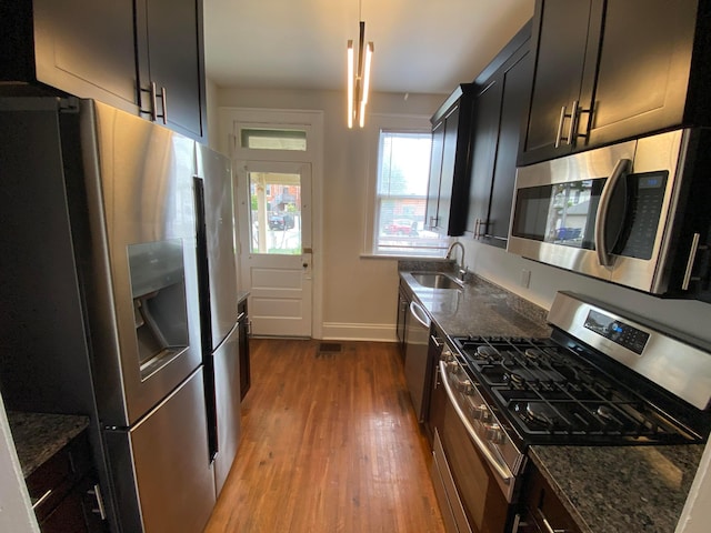 kitchen featuring appliances with stainless steel finishes, dark stone counters, sink, pendant lighting, and light hardwood / wood-style floors