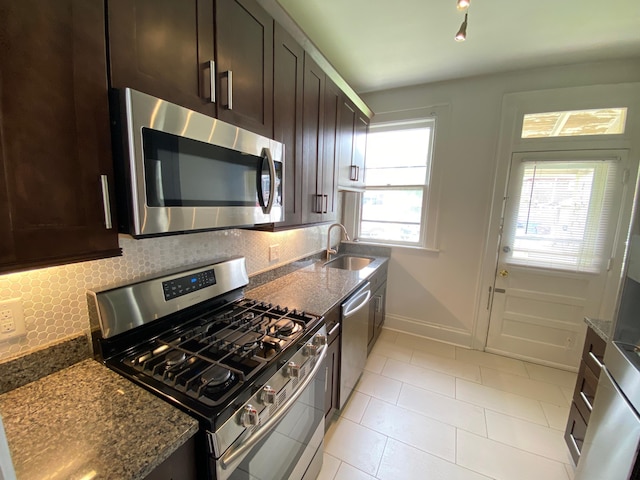 kitchen with tasteful backsplash, dark stone counters, dark brown cabinets, stainless steel appliances, and sink