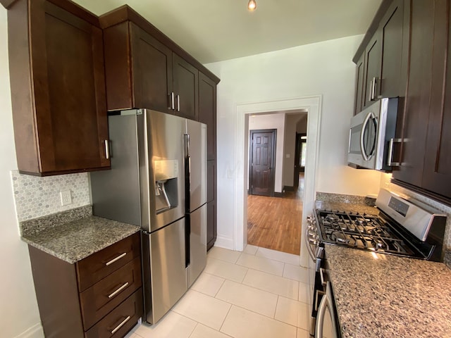 kitchen with appliances with stainless steel finishes, light wood-type flooring, backsplash, dark stone counters, and dark brown cabinets