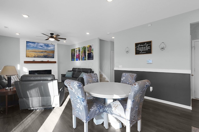 dining space featuring a large fireplace, dark hardwood / wood-style floors, and ceiling fan