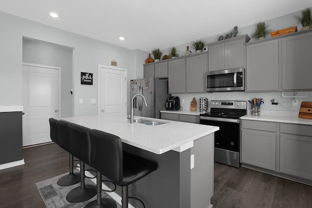 kitchen with dark wood-type flooring, stainless steel appliances, gray cabinets, and a center island with sink