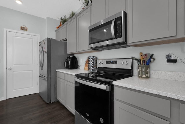 kitchen with gray cabinetry, light stone counters, dark wood-type flooring, and appliances with stainless steel finishes