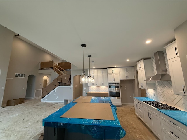 kitchen with visible vents, wall chimney range hood, arched walkways, stainless steel double oven, and gas stovetop