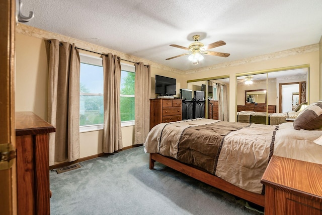 carpeted bedroom with a textured ceiling, two closets, and ceiling fan