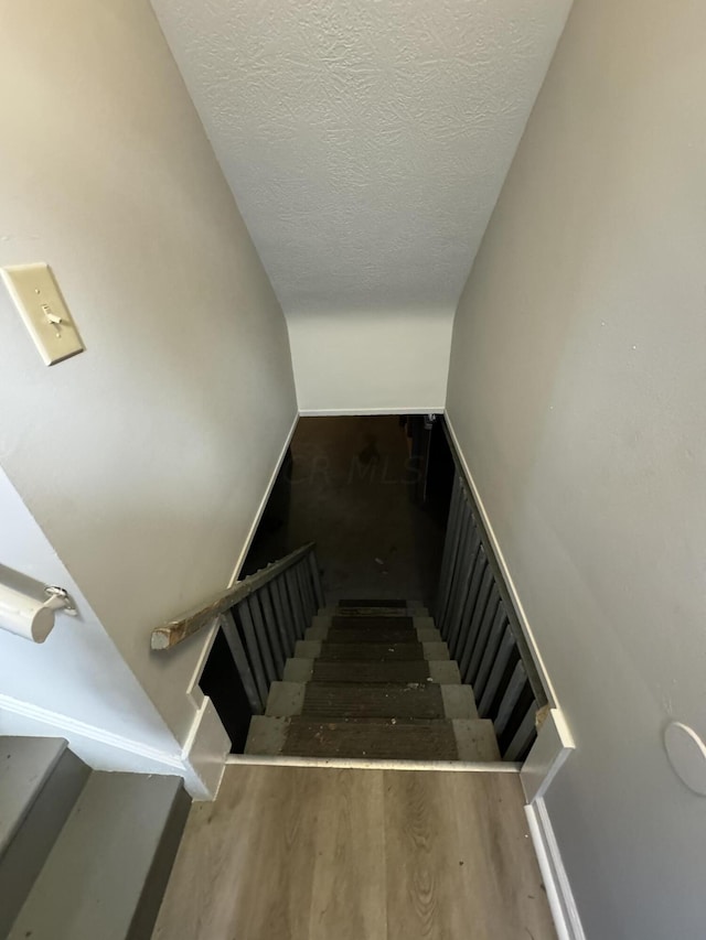 stairs with hardwood / wood-style floors, lofted ceiling, and a textured ceiling