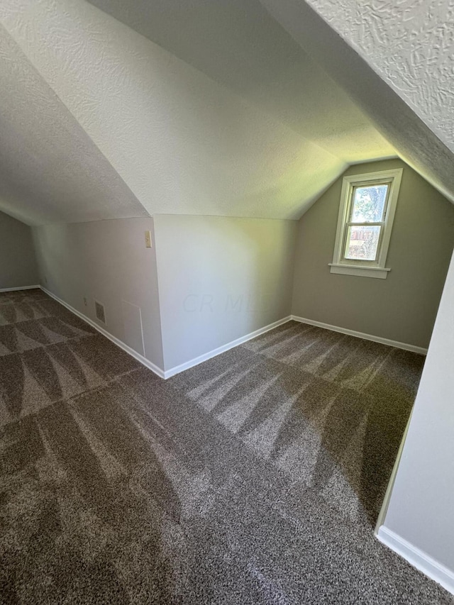 bonus room featuring dark carpet, lofted ceiling, and a textured ceiling