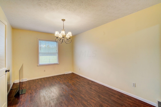 unfurnished room with dark wood-type flooring, a textured ceiling, and a notable chandelier