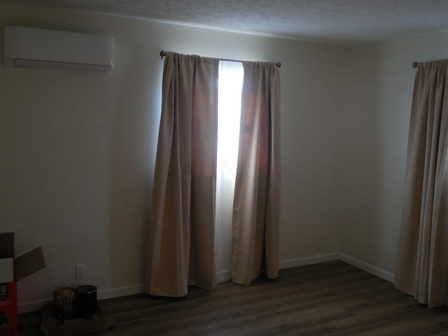 empty room featuring dark hardwood / wood-style floors, a textured ceiling, and a wall unit AC