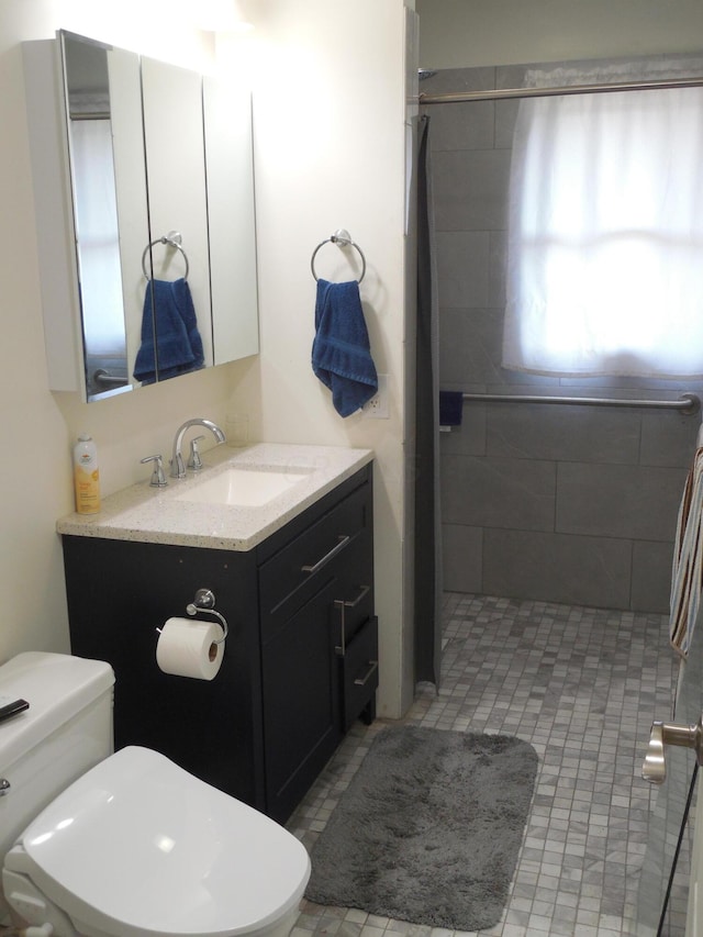 bathroom with vanity, toilet, and tiled shower