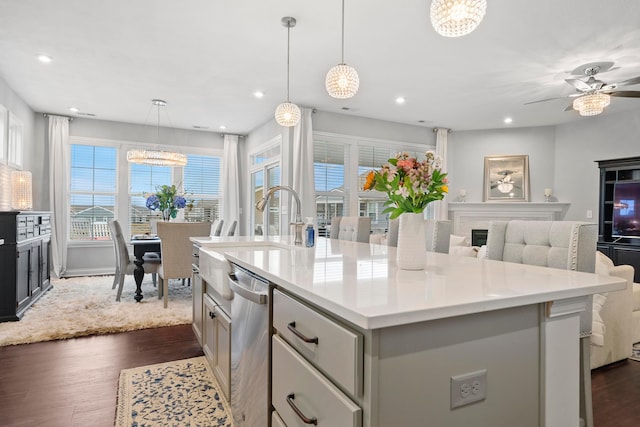 kitchen with pendant lighting, dishwasher, a kitchen island with sink, ceiling fan with notable chandelier, and dark hardwood / wood-style floors