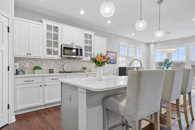 kitchen featuring appliances with stainless steel finishes, dark hardwood / wood-style flooring, a kitchen island with sink, decorative light fixtures, and white cabinetry