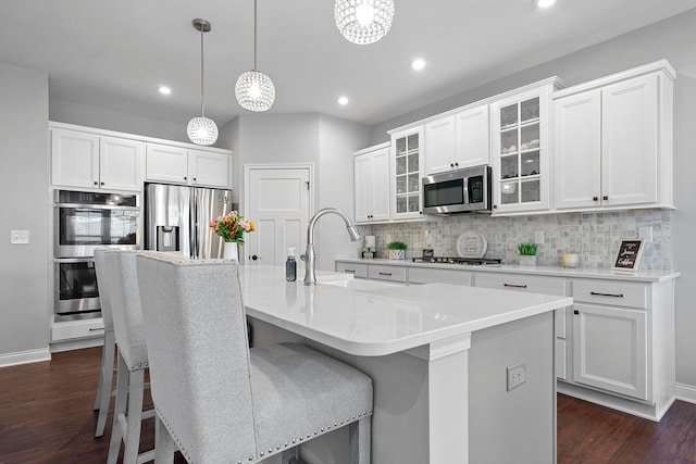 kitchen with a kitchen island with sink, sink, pendant lighting, and appliances with stainless steel finishes