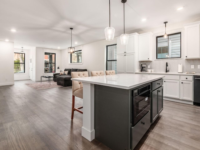 kitchen featuring pendant lighting, a center island, black appliances, light wood-type flooring, and white cabinetry