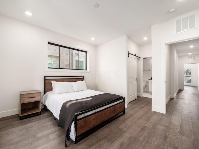 bedroom with wood-type flooring, a barn door, and connected bathroom