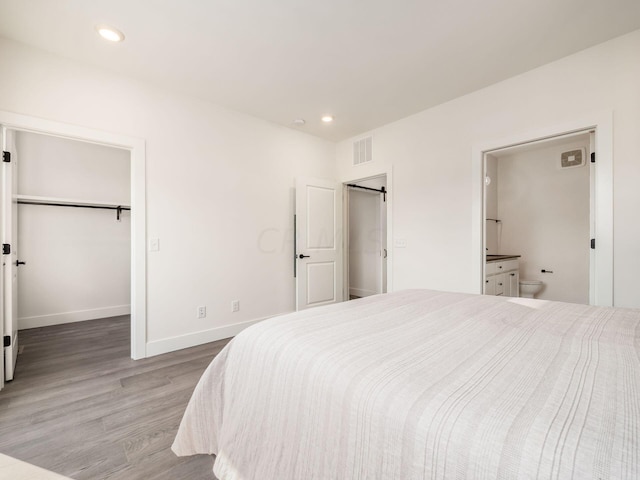 bedroom with hardwood / wood-style floors, a walk in closet, connected bathroom, and a closet